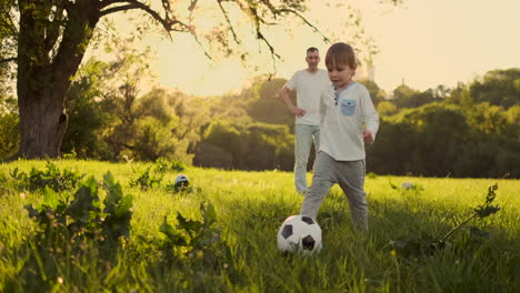 Father-standing-at-the-gate-playing-football-with-his-son-at-sunset.-The-father-trains-the-child-on-the-field.-Boy-strikes-the-ball